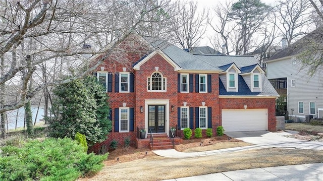 colonial home featuring concrete driveway, a shingled roof, a garage, brick siding, and central AC unit
