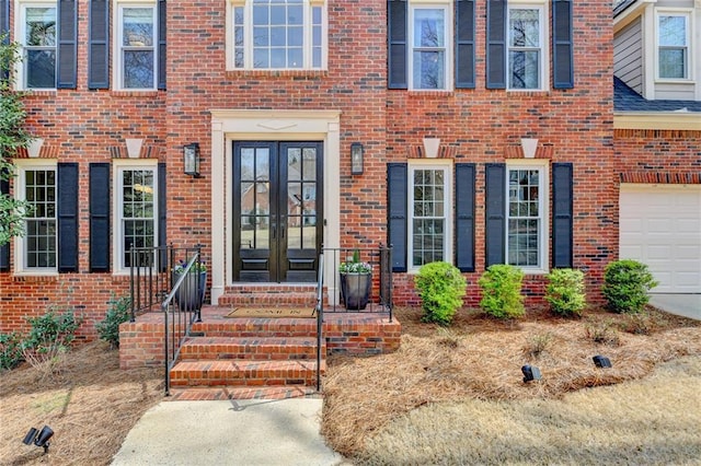view of exterior entry with french doors, brick siding, and a garage