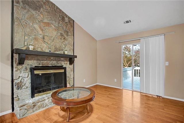 living room featuring visible vents, vaulted ceiling, a stone fireplace, wood finished floors, and baseboards