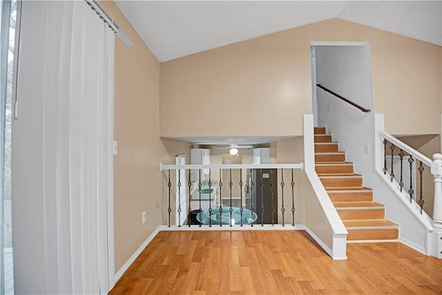 stairway featuring a ceiling fan, lofted ceiling, baseboards, and wood finished floors