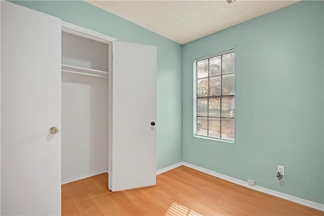 unfurnished bedroom with light wood finished floors, a closet, baseboards, and a textured ceiling