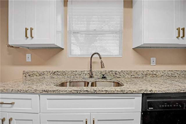 kitchen with light stone counters, white cabinetry, dishwasher, and a sink