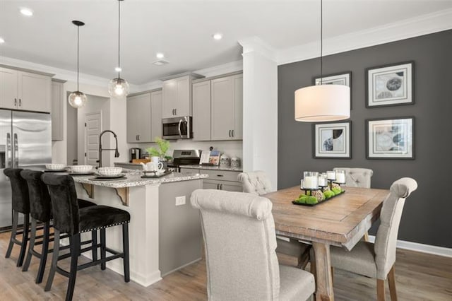 kitchen featuring a breakfast bar, crown molding, stainless steel appliances, gray cabinets, and light wood-style flooring