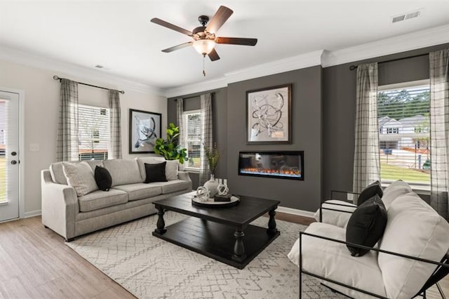 living area featuring plenty of natural light, a glass covered fireplace, visible vents, and crown molding