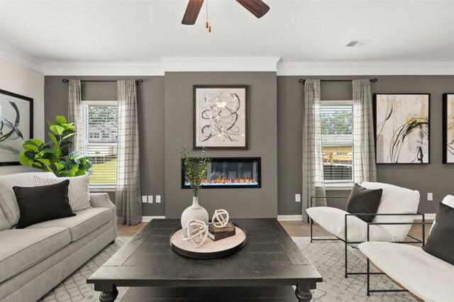 living room with ornamental molding, a glass covered fireplace, plenty of natural light, and light wood-style flooring