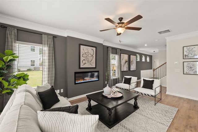 living area featuring wood finished floors, a glass covered fireplace, visible vents, and crown molding