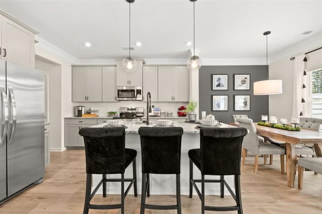 kitchen with stainless steel appliances, a kitchen breakfast bar, ornamental molding, light stone countertops, and an island with sink