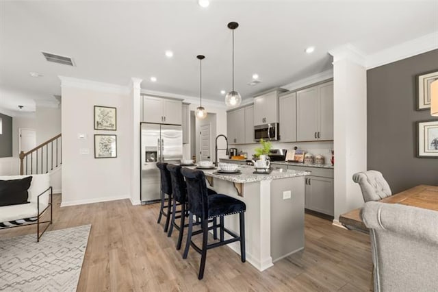 kitchen featuring appliances with stainless steel finishes, a kitchen breakfast bar, a kitchen island with sink, crown molding, and gray cabinetry