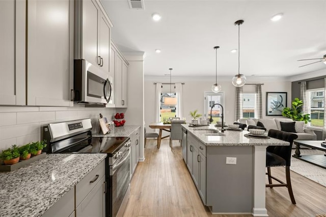 kitchen with stainless steel appliances, a sink, light wood-style floors, open floor plan, and gray cabinets