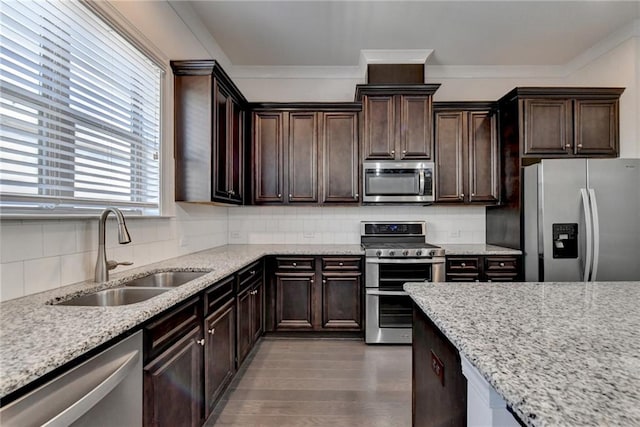 kitchen with light stone counters, sink, appliances with stainless steel finishes, dark brown cabinets, and backsplash