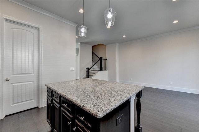 kitchen featuring light stone counters, a center island, dark hardwood / wood-style floors, hanging light fixtures, and ornamental molding