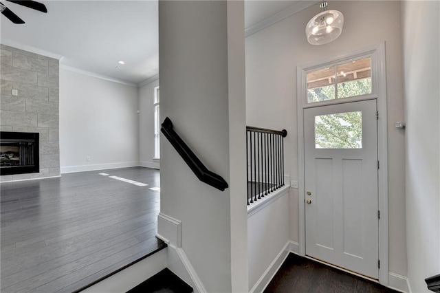 foyer with ornamental molding, a tiled fireplace, and dark wood-type flooring