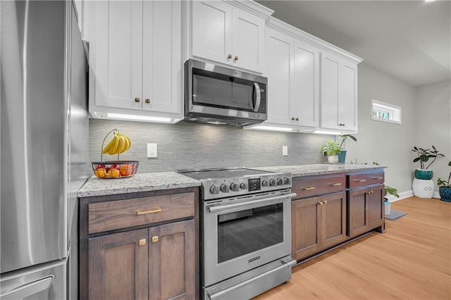 kitchen with white cabinets, light wood-type flooring, light stone countertops, tasteful backsplash, and stainless steel appliances