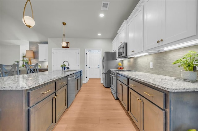 kitchen featuring light stone countertops, white cabinetry, sink, pendant lighting, and appliances with stainless steel finishes