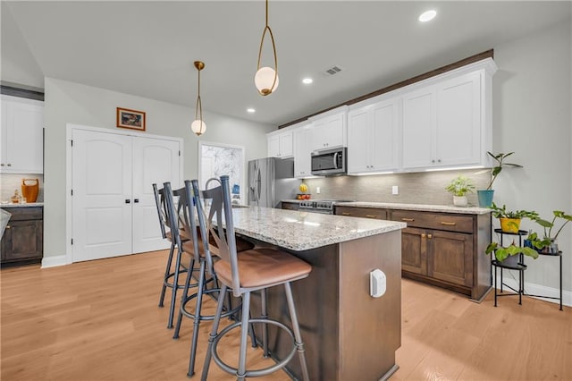 kitchen featuring a breakfast bar, white cabinets, hanging light fixtures, light hardwood / wood-style floors, and stainless steel appliances