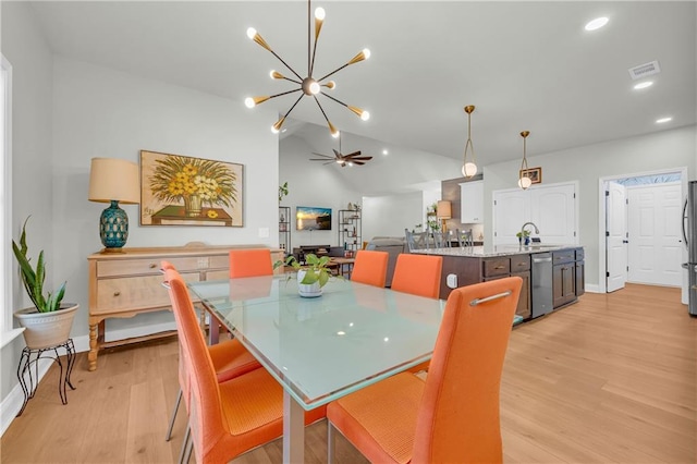 dining room with light wood-type flooring, ceiling fan with notable chandelier, lofted ceiling, and sink