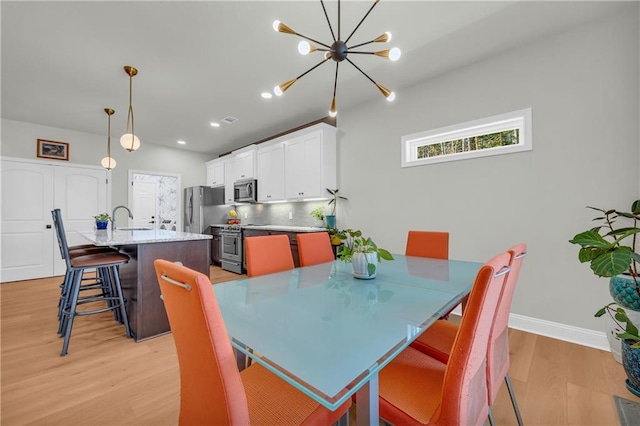 dining space with light hardwood / wood-style floors, sink, and an inviting chandelier