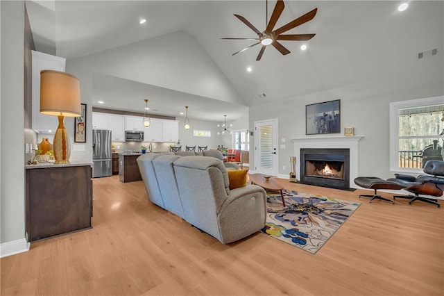 living room featuring ceiling fan with notable chandelier, light wood-type flooring, and high vaulted ceiling