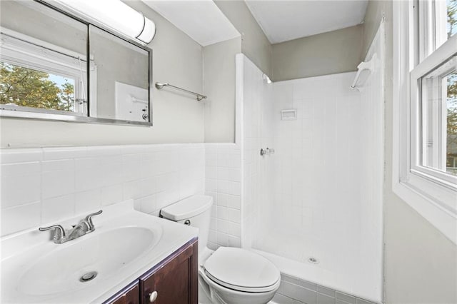 bathroom with toilet, a tile shower, tile walls, and vanity