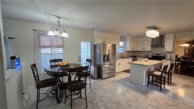 kitchen with white cabinets, stainless steel appliances, a chandelier, and wall chimney range hood