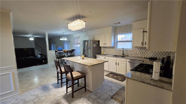 kitchen with a kitchen island, appliances with stainless steel finishes, pendant lighting, sink, and light stone counters