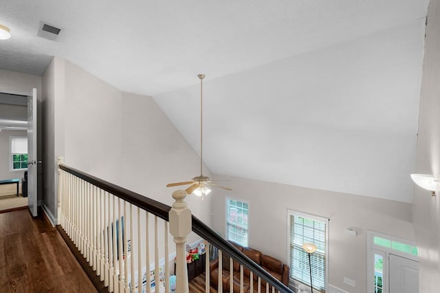 corridor with vaulted ceiling, a wealth of natural light, wood finished floors, and visible vents