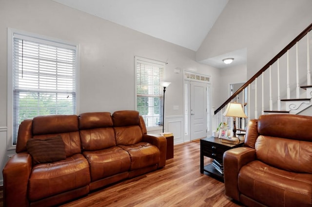 living area with stairs, a decorative wall, light wood-style floors, a wainscoted wall, and vaulted ceiling