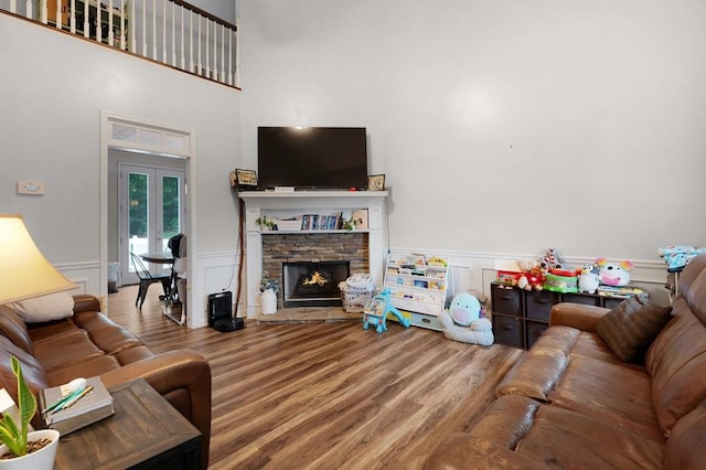 living room with a towering ceiling, a fireplace, wainscoting, wood finished floors, and a decorative wall