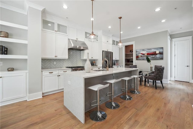 kitchen with pendant lighting, stainless steel fridge, white cabinetry, light hardwood / wood-style flooring, and an island with sink