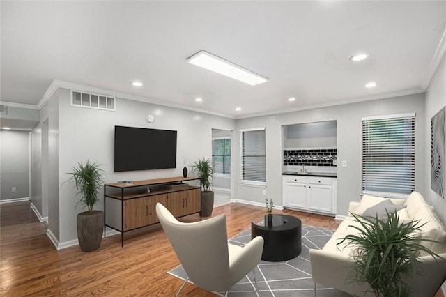 living room featuring crown molding, sink, and light wood-type flooring