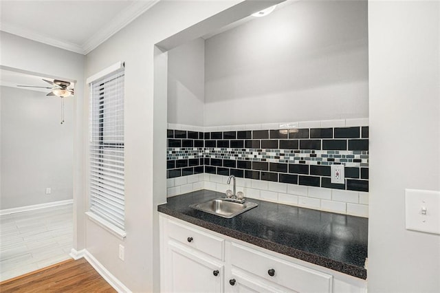 kitchen with white cabinetry, wood-type flooring, sink, backsplash, and ornamental molding