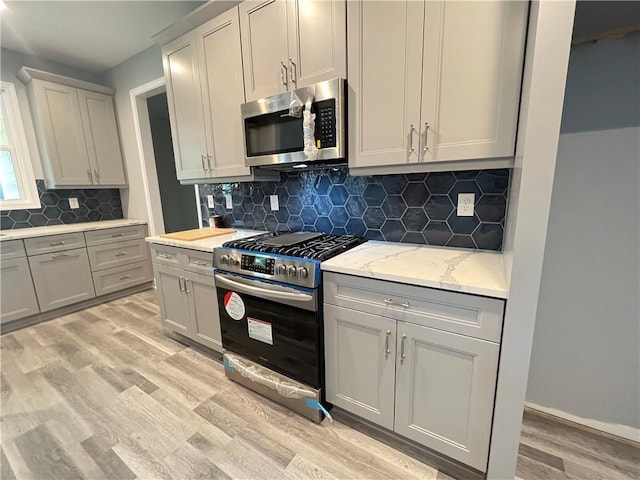154 Pope Paul Path, Dallas, GA 30132 - kitchen featuring light stone countertops, light wood-style floors, stainless steel appliances, backsplash, and gray cabinetry