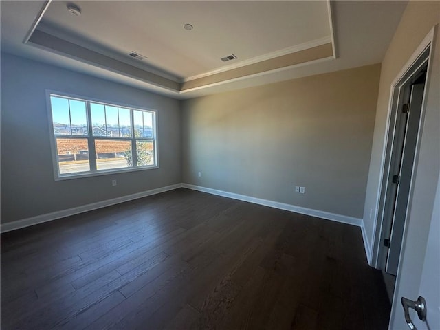 empty room featuring visible vents, baseboards, dark wood-type flooring, and a tray ceiling