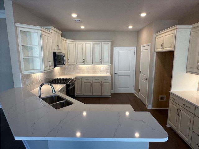 kitchen with a sink, stainless steel microwave, a peninsula, and light stone countertops