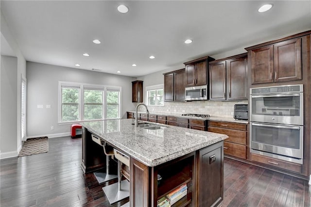 5770 Bridleton Xing, Suwanee, GA 30024 - kitchen featuring stainless steel appliances, a sink, a kitchen island with sink, dark wood finished floors, and light stone counters