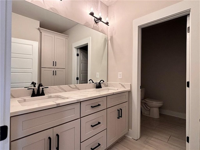 bathroom featuring toilet, double vanity, baseboards, and a sink