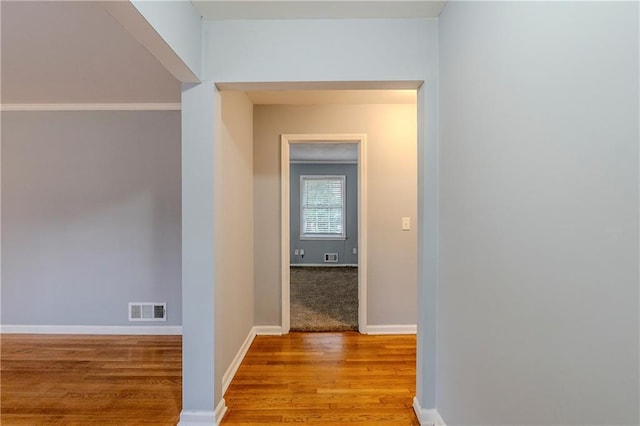 hall with baseboards, visible vents, and wood finished floors