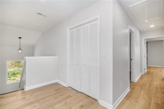 corridor featuring attic access, light wood-style flooring, and baseboards