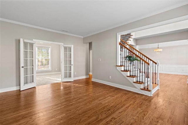 unfurnished living room with stairs, an inviting chandelier, wood finished floors, and crown molding