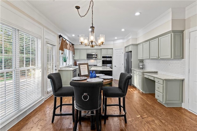 dining area with ornamental molding, wood finished floors, an inviting chandelier, built in desk, and recessed lighting