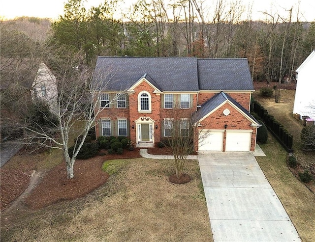 colonial inspired home with a garage, driveway, brick siding, and a front yard