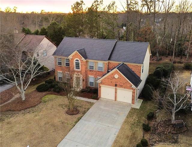 colonial inspired home with concrete driveway, brick siding, a wooded view, and an attached garage