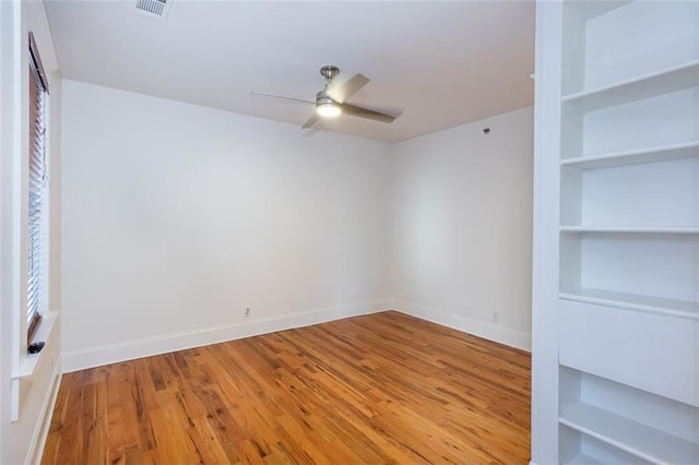 empty room featuring hardwood / wood-style flooring, built in shelves, baseboards, visible vents, and ceiling fan