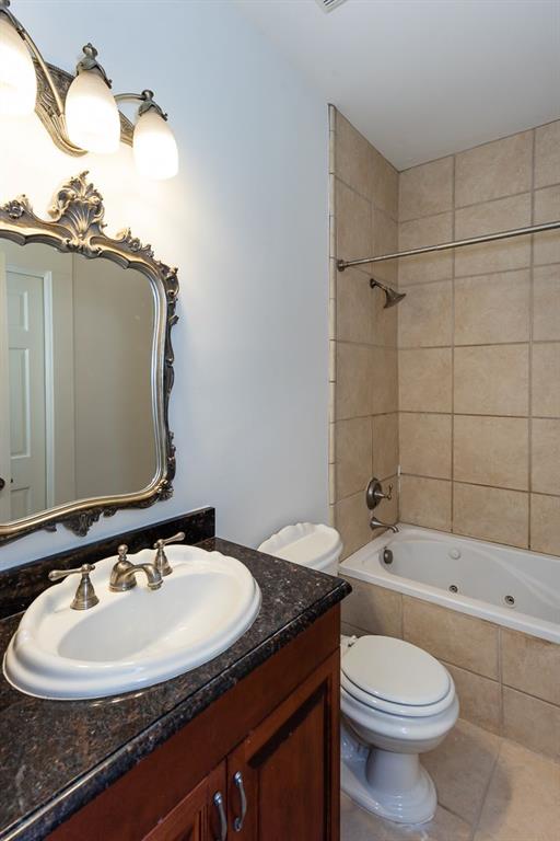 full bath with tile patterned floors, vanity, tiled shower / bath, and toilet