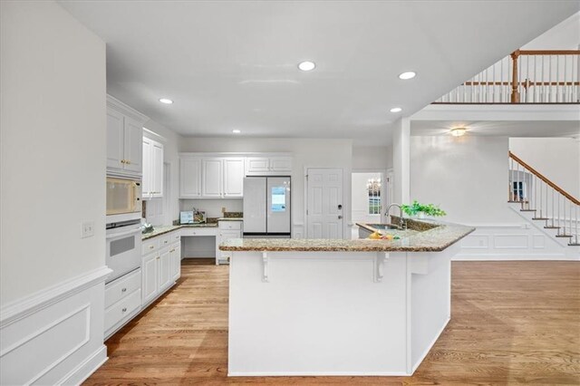 kitchen with white cabinetry, white appliances, a kitchen breakfast bar, and sink