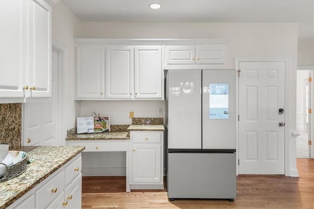 kitchen with white cabinetry, built in desk, light stone countertops, and white fridge