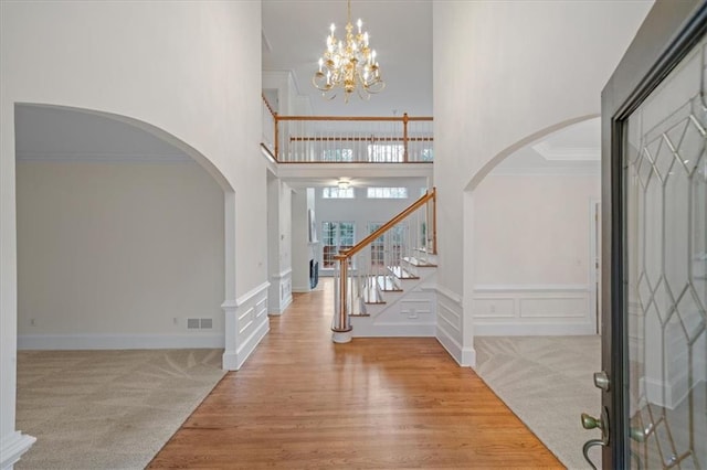 carpeted entryway featuring a notable chandelier, a towering ceiling, and ornamental molding