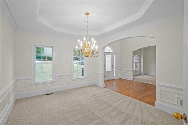 unfurnished room featuring an inviting chandelier, crown molding, light colored carpet, and a raised ceiling