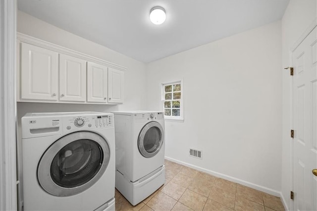 clothes washing area with cabinets, washing machine and clothes dryer, and light tile patterned floors