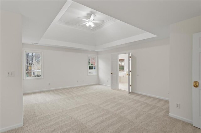 empty room with ceiling fan, light colored carpet, plenty of natural light, and a tray ceiling